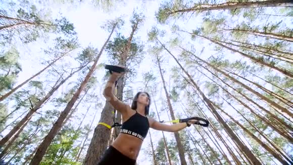 运动女性教练教练表演做运动与健身TRX系统TRX悬挂带松树视频的预览图