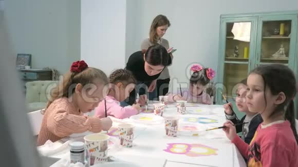 孩子们男孩和女孩在教室里围着桌子坐在一起画画与他们在一起的是他们的年轻视频的预览图