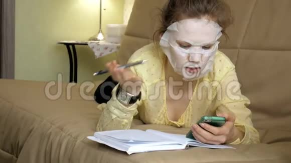 年轻女性在家里用智能手机点击沙发上的清洁面膜视频的预览图