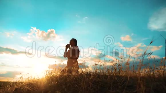 女孩在日落时双手交叉祈祷剪影女人的生活方式跪着祈祷慢动作视频女孩视频的预览图