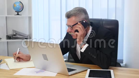 办公室里的老人用白色智能手机说话视频的预览图