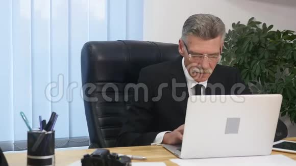 在现代办公室用电脑工作的老商人视频的预览图