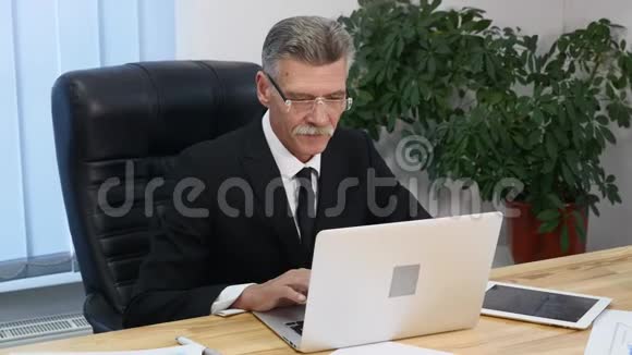 在现代办公室用电脑工作的老商人视频的预览图