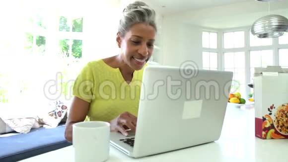 美国黑人妇女在家庭厨房里使用笔记本电脑视频的预览图