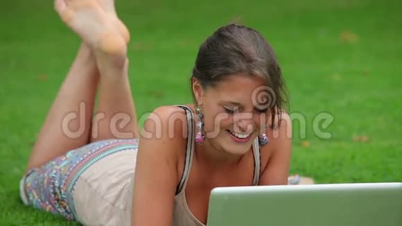 微笑的学生躺在草地上用笔记本电脑视频的预览图