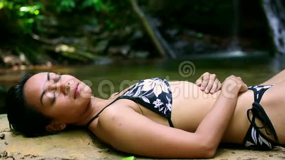 穿比基尼的女孩躺在瀑布河里视频的预览图