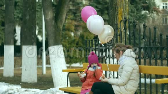 一个漂亮的女孩和她的妈妈坐在公园的长凳上吃着美味的甜点喝着热水瓶里的茶视频的预览图