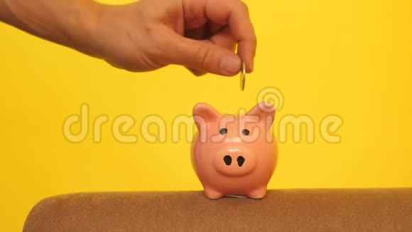 猪银行的经营理念一只手把硬币放在黄色背景上的储蓄罐里省钱就是视频的预览图