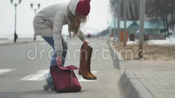 年轻漂亮的女人戴着红帽子穿着运动温暖的衣服和滚筒骑在海岸上的路上视频的预览图