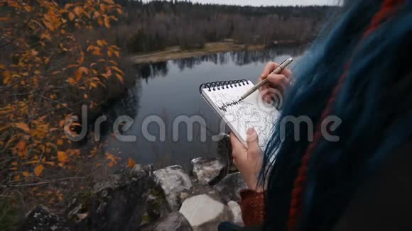 艺术家女孩画坐在悬崖的岩石上记事本奇妙的瀑布景观视频的预览图