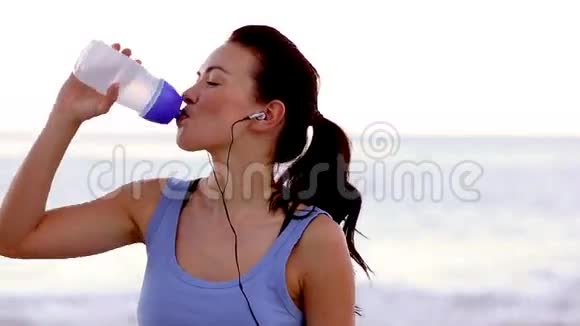 女人在沙滩上喝水对着镜头微笑视频的预览图