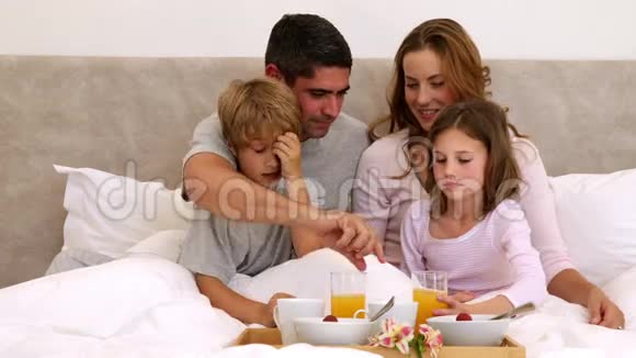 可爱的父母和孩子在床上吃早餐视频的预览图