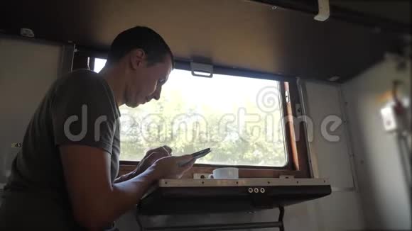 这名男子坐在火车铁路车厢上手里拿着一部智能手机生活方式是喝咖啡和茶慢动作视频的预览图