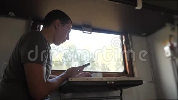 这名男子坐在火车铁路车厢上手里拿着一部智能手机喝着生活方式咖啡和茶慢动作视频的预览图