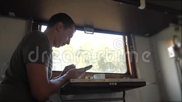 这个人坐在火车铁路车厢上抱着智能手机的生活方式喝着咖啡和茶慢动作视频的预览图