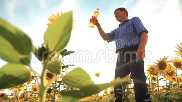 农夫老人手里拿着一个塑料瓶向日葵油立在田野里慢动作视频葵花籽油视频的预览图