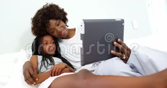 母亲和女儿在卧室里用数码平板电脑视频的预览图