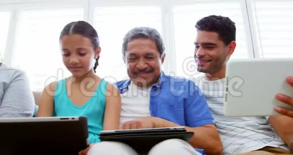 幸福的家庭坐在沙发上使用笔记本电脑手机和数字平板电脑视频的预览图