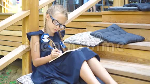 可爱的小女孩带着笔记和铅笔在户外回学校去视频的预览图