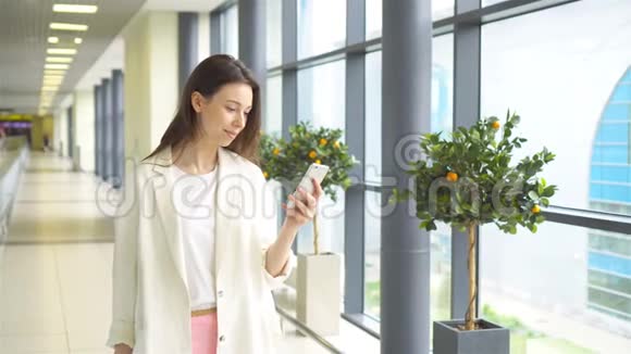 在国际机场带智能手机的旅游女孩在机场休息室等候航班的航空公司乘客视频的预览图