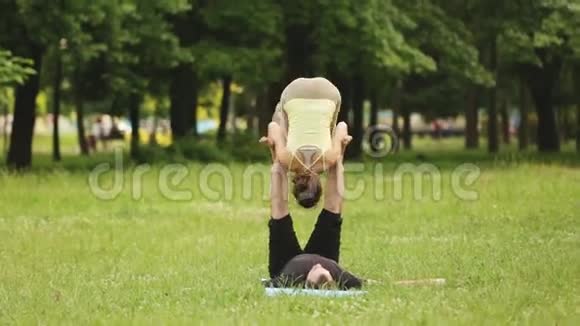 漂亮的一对练习杂技瑜伽年轻的瑜伽教练在绿草如茵的城市公园练习两次成功视频的预览图