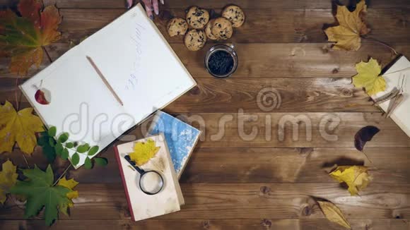 秋季概念俯视图书枫叶旧木桌上的茶女人在笔记本上写笔记视频的预览图