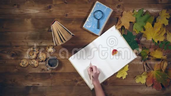秋季概念俯视图书枫叶旧木桌上的茶女人在笔记本上写笔记视频的预览图
