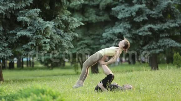 漂亮的一对练习杂技瑜伽年轻的瑜伽教练在绿草如茵的城市公园练习两次成功视频的预览图