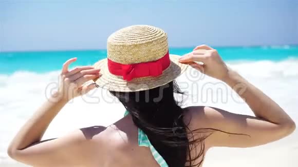 戴帽子的年轻女子在热带海滩上看着美丽的大海视频的预览图