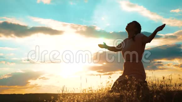 女孩在日落时双手交叉祈祷剪影女人跪着祈祷慢动作视频女孩视频的预览图