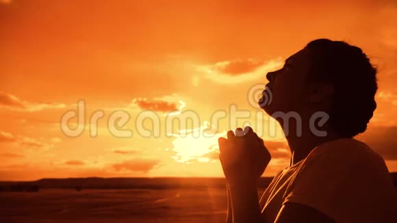 女孩祈祷女孩在日落时双手交叉祈祷剪影生活方式慢动作视频女孩双手合拢视频的预览图
