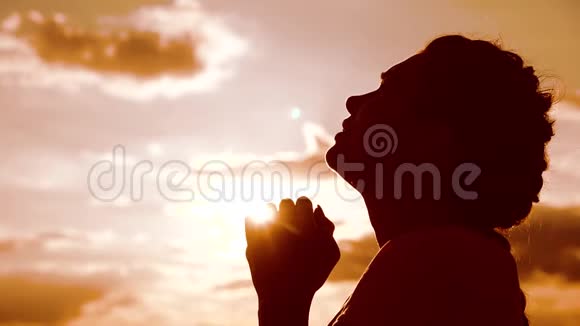 女孩祈祷女孩在日落时双手交叉祈祷剪影慢动作视频女孩双手合拢视频的预览图