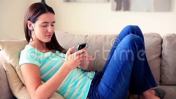 漂亮的黑发女人在沙发上听音乐放松视频的预览图