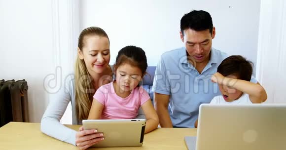 在客厅里使用数码平板电脑和笔记本电脑的幸福家庭视频的预览图