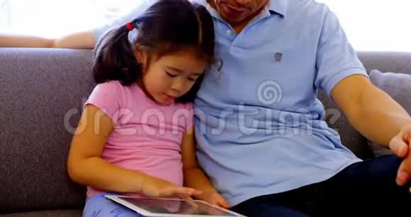 父亲和女儿在客厅里用数码平板电脑视频的预览图