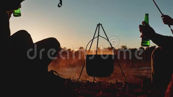 两名游客的生活方式是坐在篝火晚会上在大自然中露营剪影阳光日落两个男人剪影视频的预览图