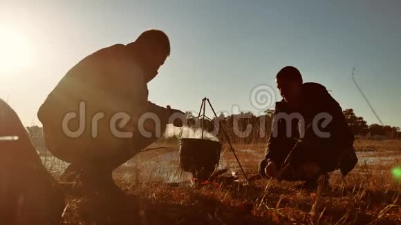 两名游客啤酒正坐着生活方式篝火徒步聚会在大自然中露营剪影阳光日落两个人视频的预览图