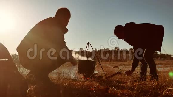 两位游客啤酒正坐在生活方式篝火徒步聚会上在大自然露营剪影阳光下日落两个人视频的预览图