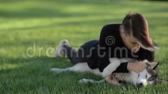 美丽的年轻女子在草地上的公园里玩有趣的哈士奇狗视频的预览图