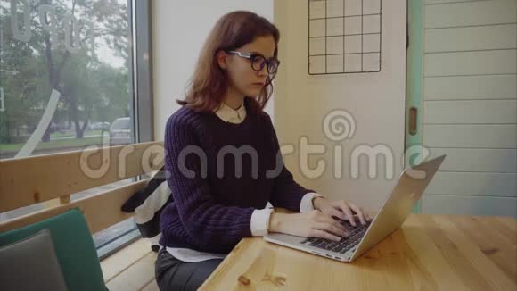 年轻女学生带着现代笔记本电脑坐在咖啡馆里视频的预览图