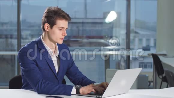 年轻商人在办公室坐在办公桌旁的笔记本电脑的肖像视频的预览图