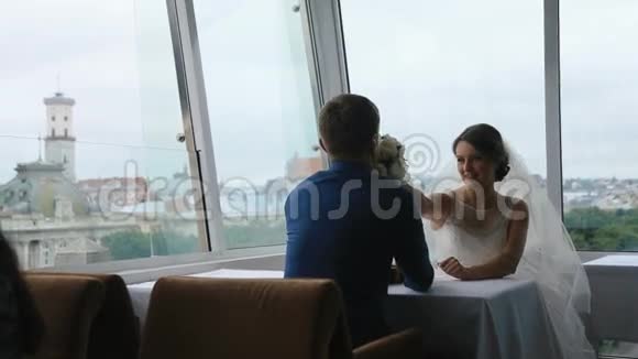 快乐的年轻新娘给新郎闻玫瑰花束在一家咖啡馆与全景城市的背景视频的预览图