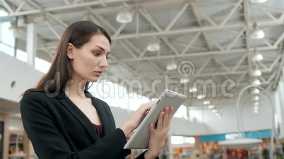年轻的女旅客在机场等待航班时使用她的平板电脑商务女性之后视频的预览图