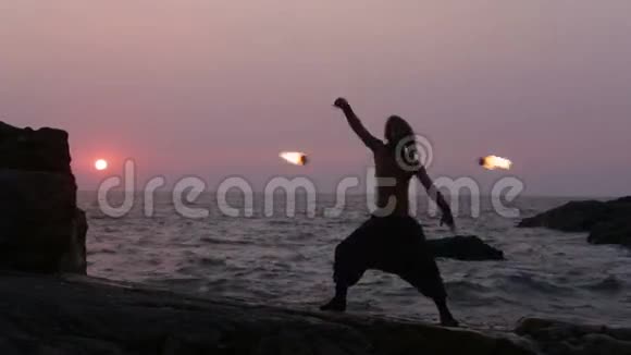 日落时分站在靠近海洋的悬崖上的人转过火堆视频的预览图