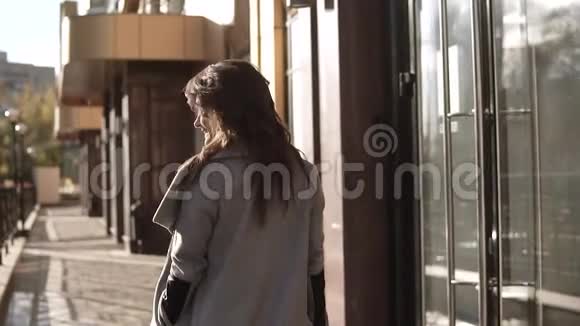 迷人的年轻女子穿着外套微笑着穿过秋天的城市现代社会背景下的可爱女孩视频的预览图