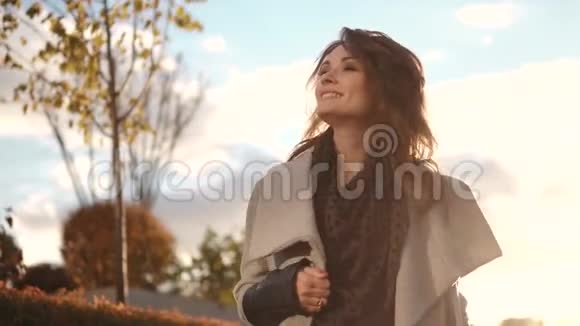 迷人的年轻女子穿着外套微笑着穿过秋天的城市视频的预览图