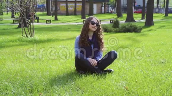 美丽的年轻女子坐在夏日公园的草地上视频的预览图