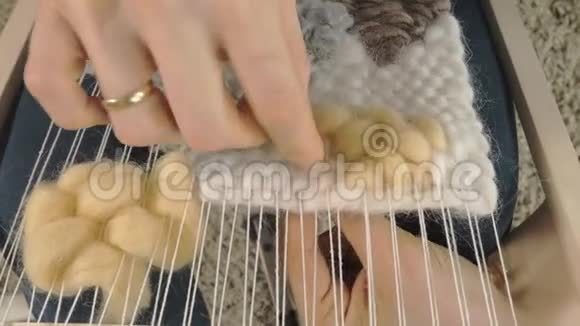 一个女人在织布机上织着一件由纱线制成的美丽刺绣在一个家庭工作室里视频的预览图