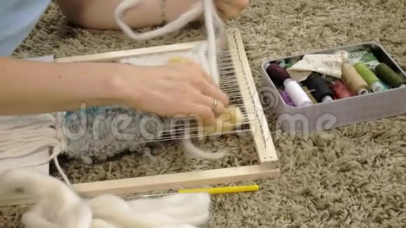 一个女人在织布机上织着一件由纱线制成的美丽刺绣在一个家庭工作室里视频的预览图