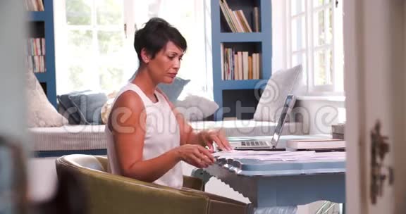 在家庭办公室工作的成熟妇女带手提电脑视频的预览图